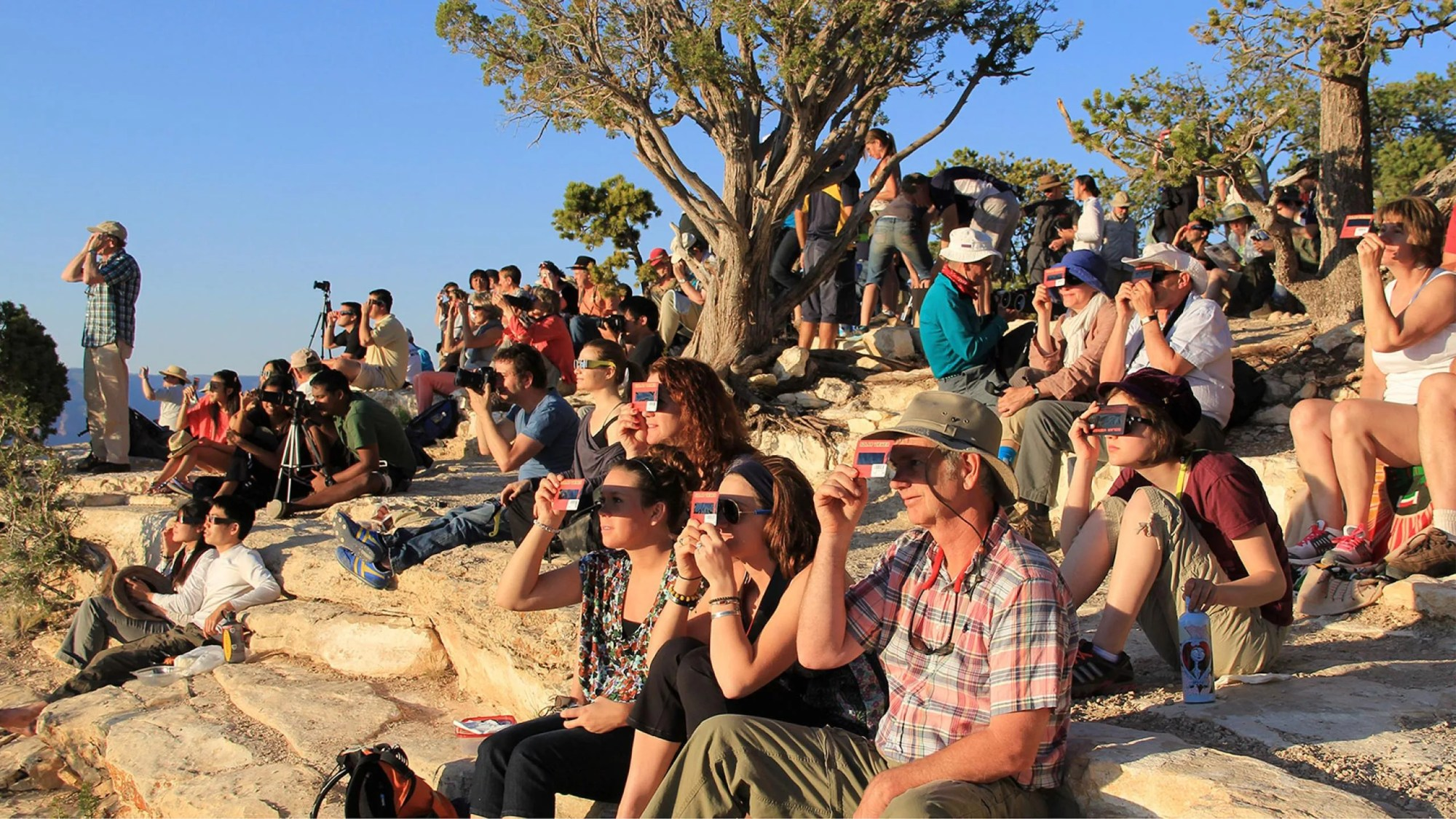 Imagen de una multitud de personas utilizando visores solares de mano y anteojos para eclipses solares para observar con seguridad un eclipse solar.