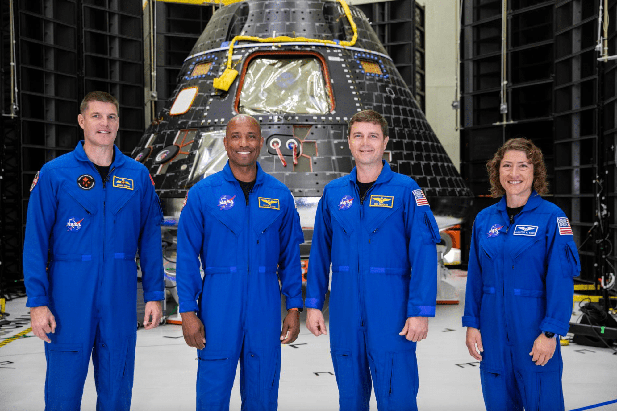 Los cuatro integrantes de la tripulación de Artemis II aparecen aquí de pie frente a su módulo de la tripulación de la nave espacial Orion el día 8 de agosto de 2023, dentro del Edificio de Operaciones y Comprobación Neil Armstrong en el Centro Espacial Kennedy de la NASA en Florida. Visten el mono azul de astronauta.