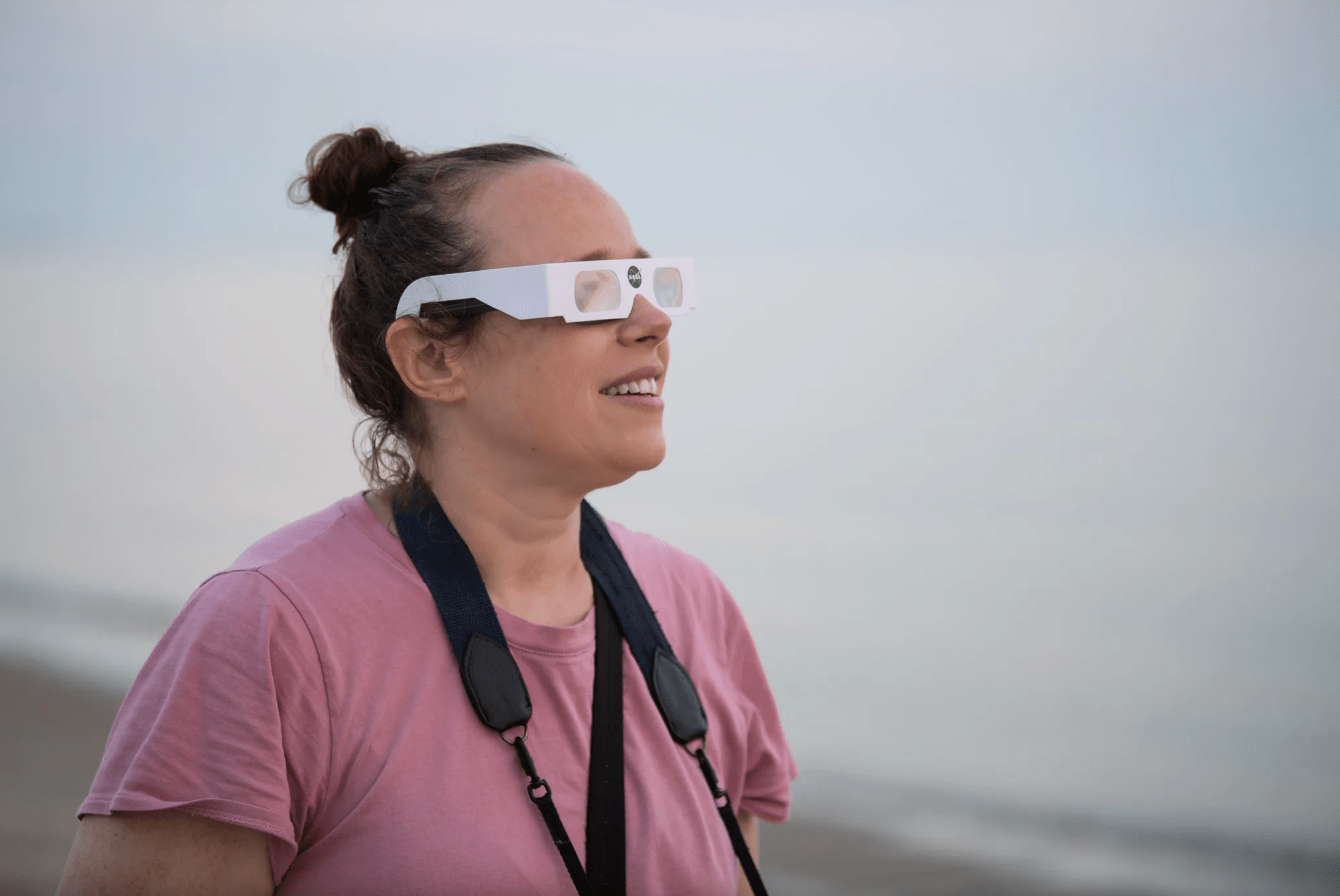 Sarah Baker, una mujer de pelo marrón recogido en un moño, observa el eclipse solar parcial durante el amanecer del jueves 10 de junio de 2021, en Lewes Beach, Delaware.