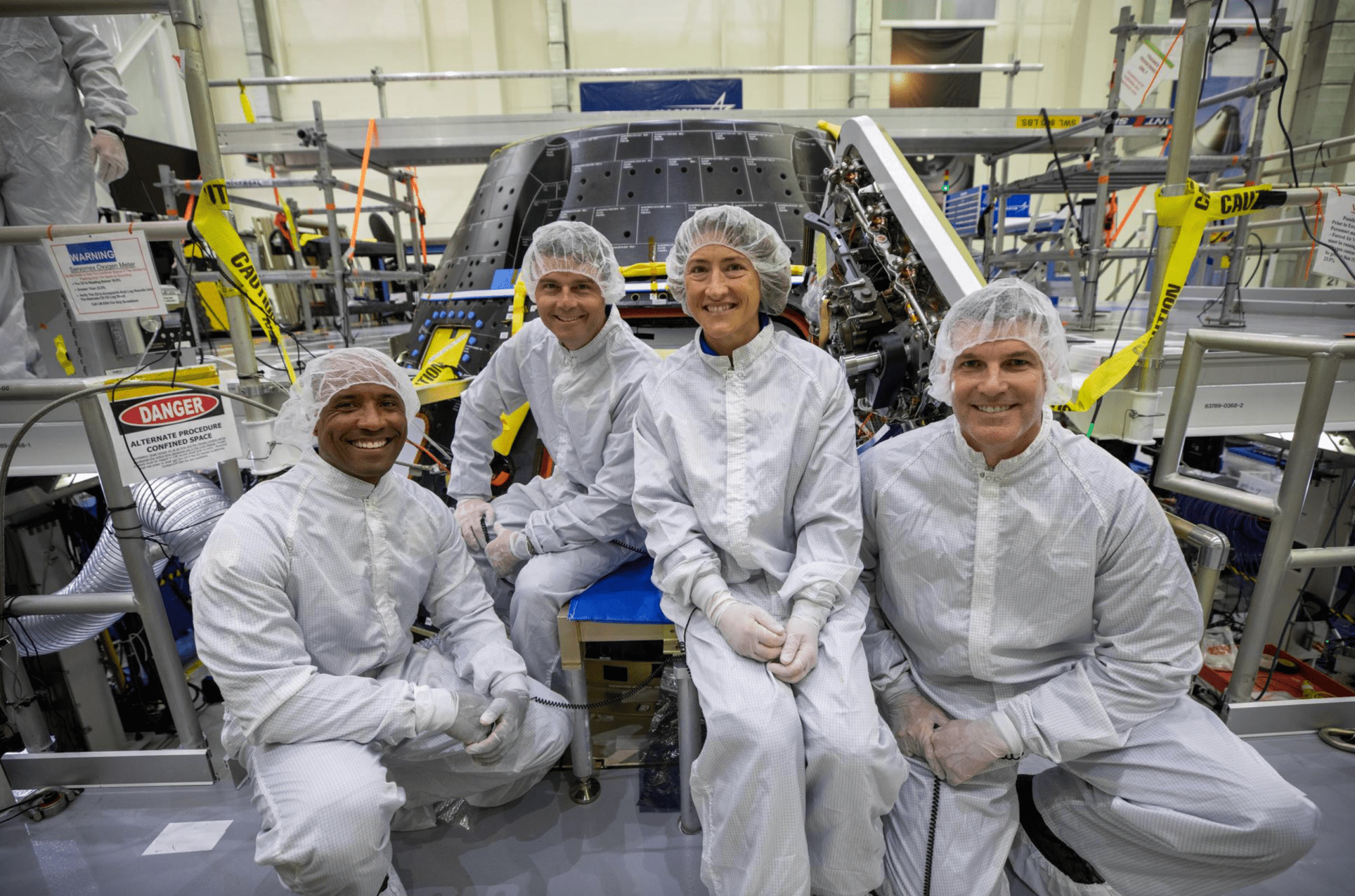 Los integrantes de la tripulación de Artemis II inspeccionan su módulo de la tripulación de Orion dentro del área de talleres del Edificio de Operaciones y Comprobación Neil A. Armstrong en el Centro Espacial Kennedy de la NASA en Florida, el 7 de agosto de 2023. Visten mono, cubrecabezas y guantes blancos.