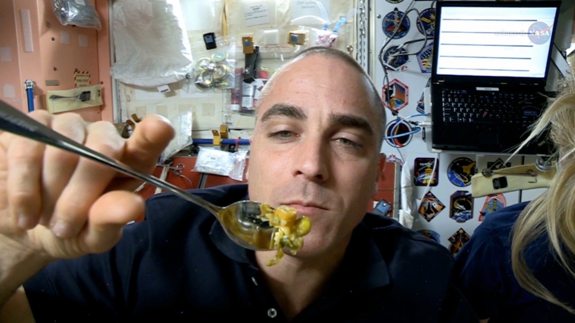 Una astronauta en la estación espacial sostiene un cubierto con comida frente a él.