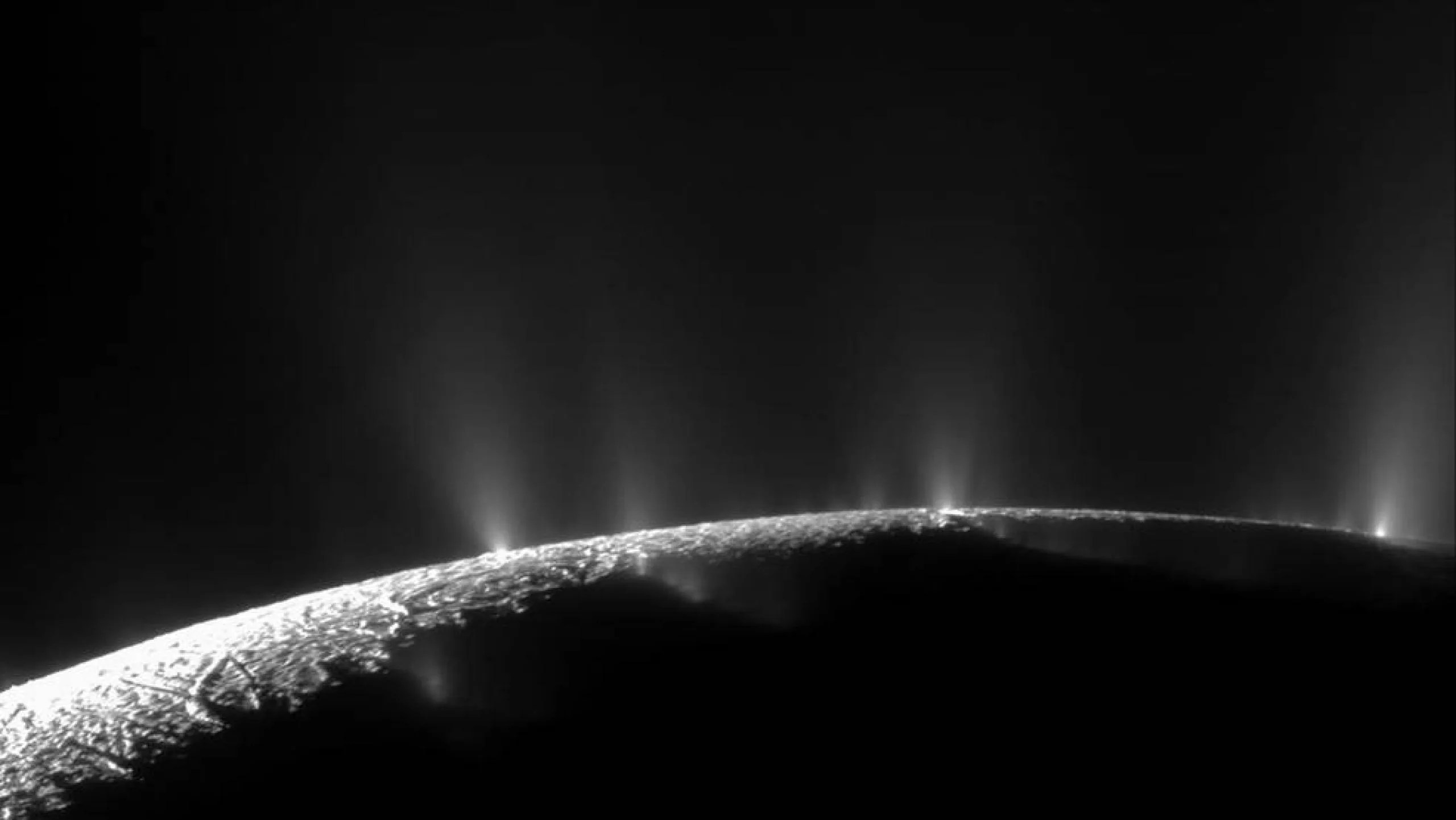 La corteza de hielo en el polo sur de Encélado muestra grandes fisuras que permiten que el agua del océano debajo de su superficie salga rociada al espacio en forma de géiseres, formando una columna de partículas congeladas.