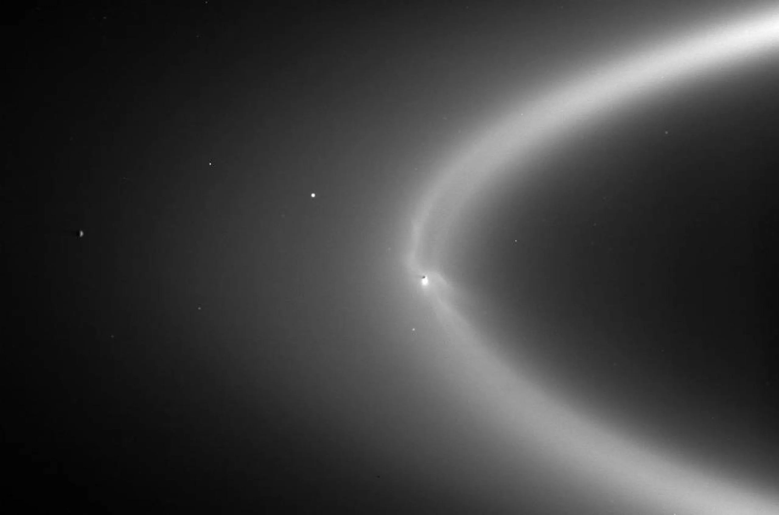 Visto como un arco brillante en esta observación de 2006 hecha por Cassini, el anillo E de Saturno se alimenta con partículas heladas de la columna de Encélado, creando tenues dedos de material brillante que es iluminado desde atrás por el Sol. El hemisferio sombreado de la luna se puede ver como un punto oscuro dentro del anillo.