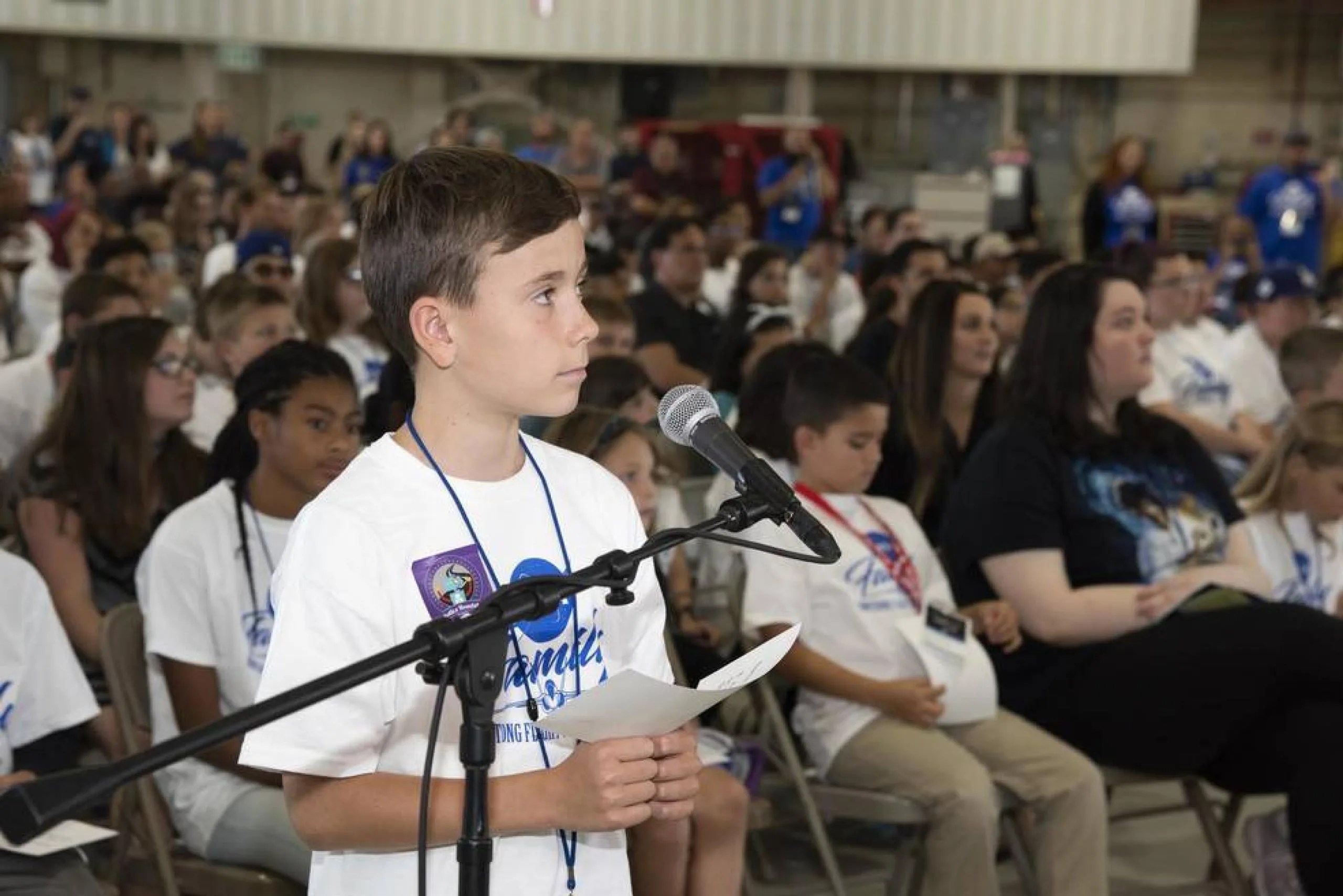 Un estudiante está de pie frente a un micrófono mientras le hace una pregunta a la astronauta de la NASA Serena M. Auñón-Chancellor durante un evento de conexión desde el espacio.