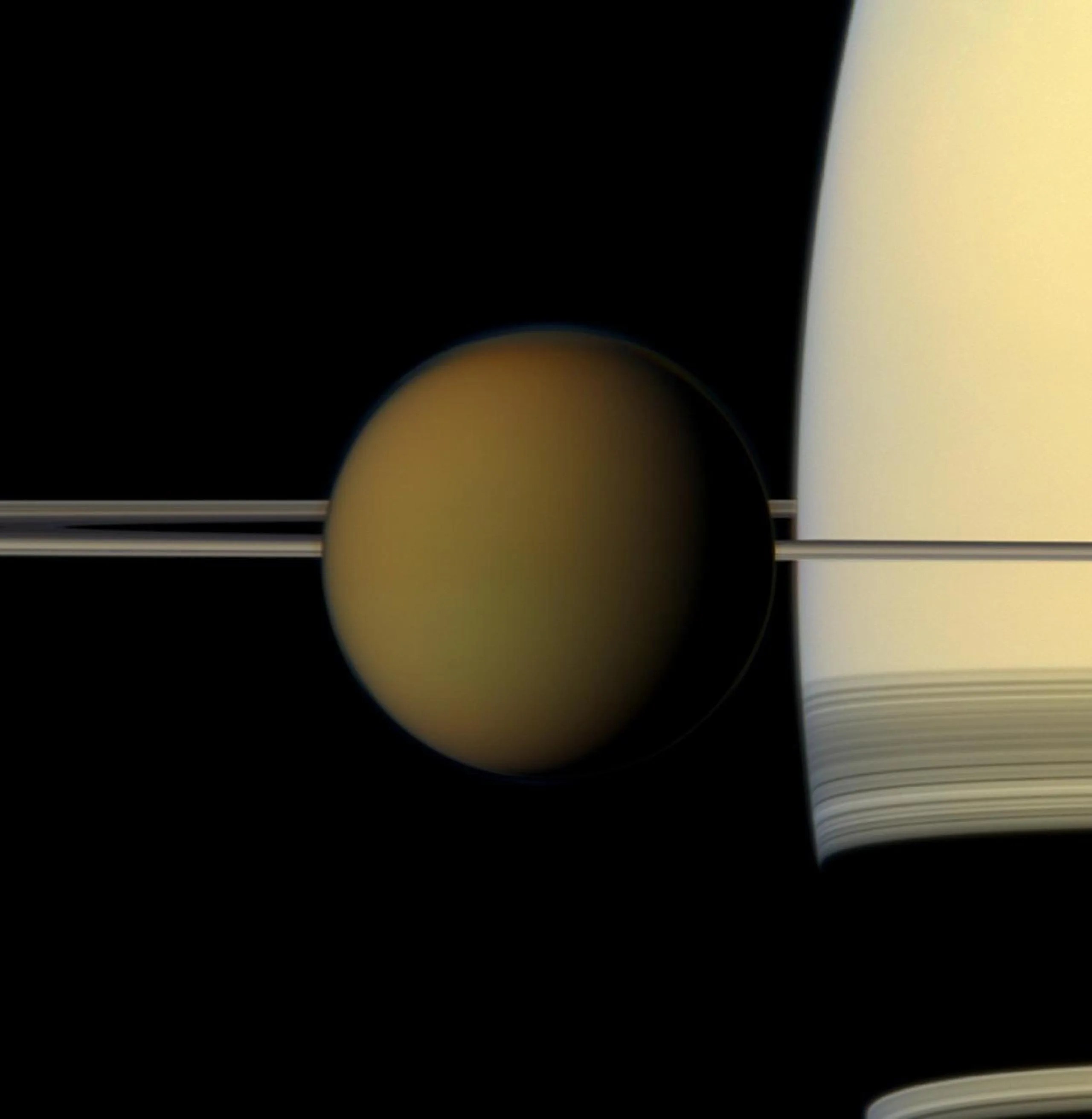 El colorido globo de la luna más grande de Saturno, Titán, pasa frente al planeta y sus anillos en esta imagen de color natural captada por la nave espacial Cassini de la NASA.