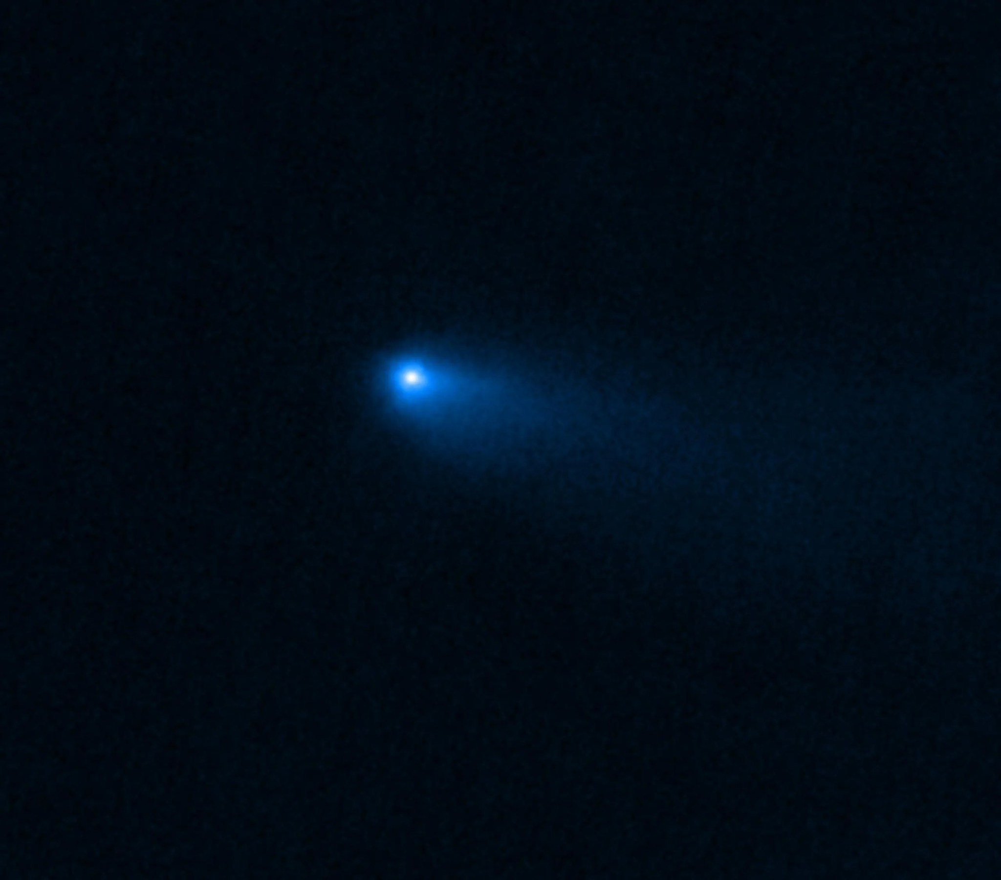 En el centro de una imagen negra, un pequeño punto brillante y brumoso resplandece con luz blanca y está rodeado de azul que se desvanece hacia la parte inferior derecha.