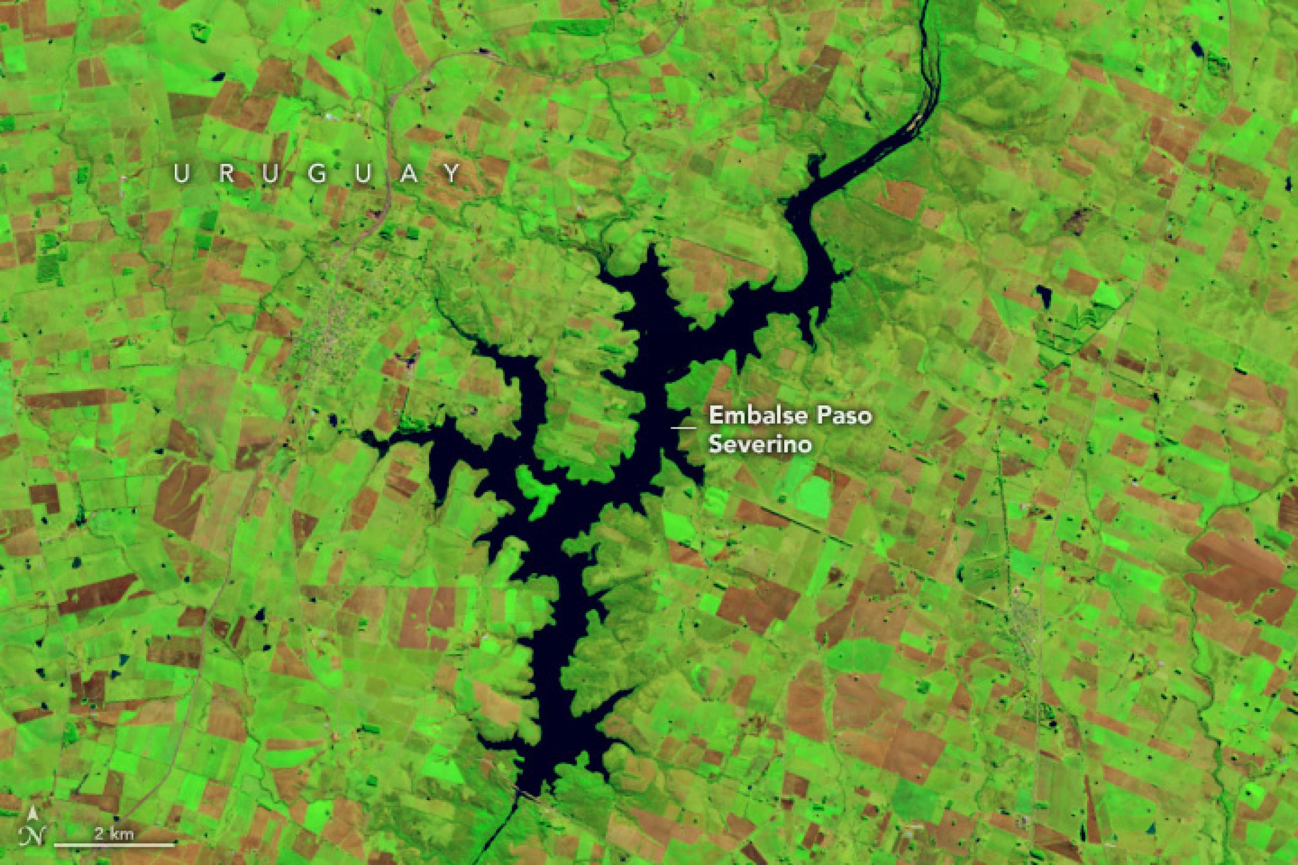 Imagen de satélite con color añadido del embalse Paso Severino en Uruguay en junio de 2022. El gran embalse en expansión es de color azul oscuro y el paisaje circundante  se ve de color verde brillante y marrón rojizo.