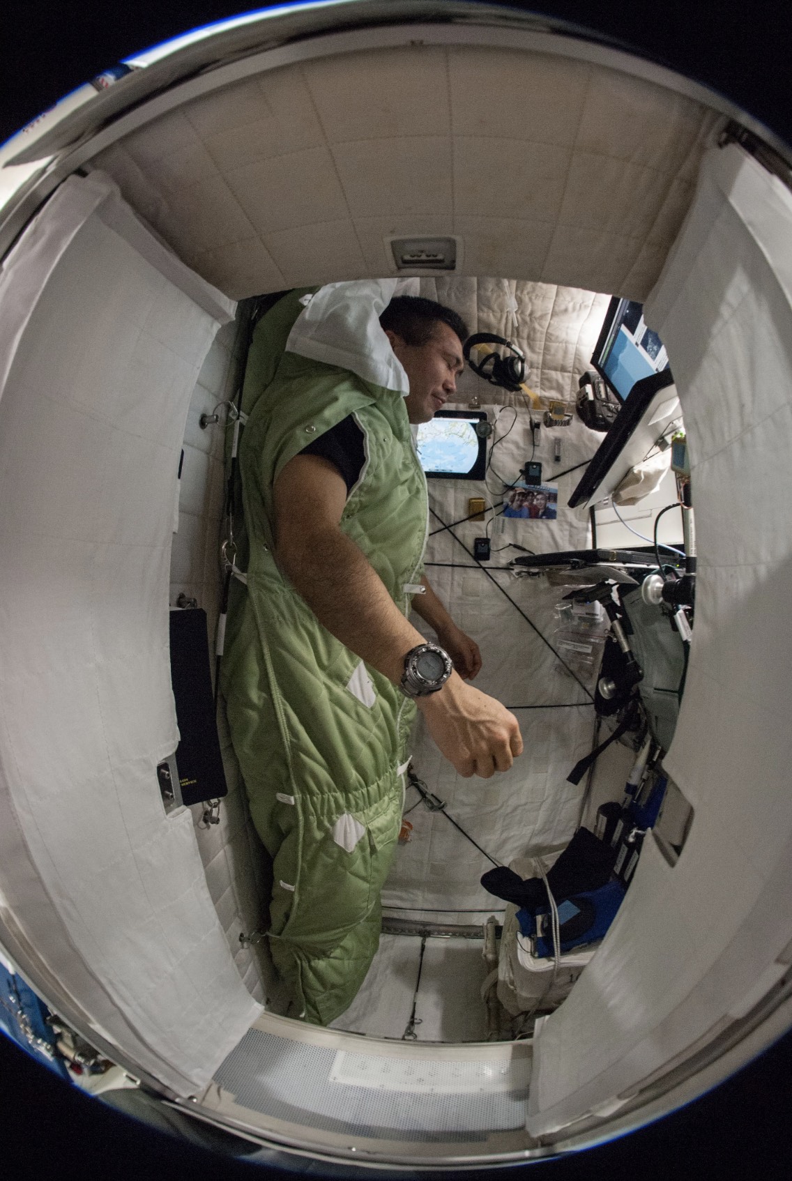 Vista del astronauta de JAXA (Agencia Japonesa de Exploración Aeroespacial) Koichi Wakata, ingeniero de vuelo de la Expedición 38, amarrado a su saco de dormir de color verde dentro de su estación para dormir ubicada en el Nodo 2. En la imagen, se ve al astronauta en vertical.