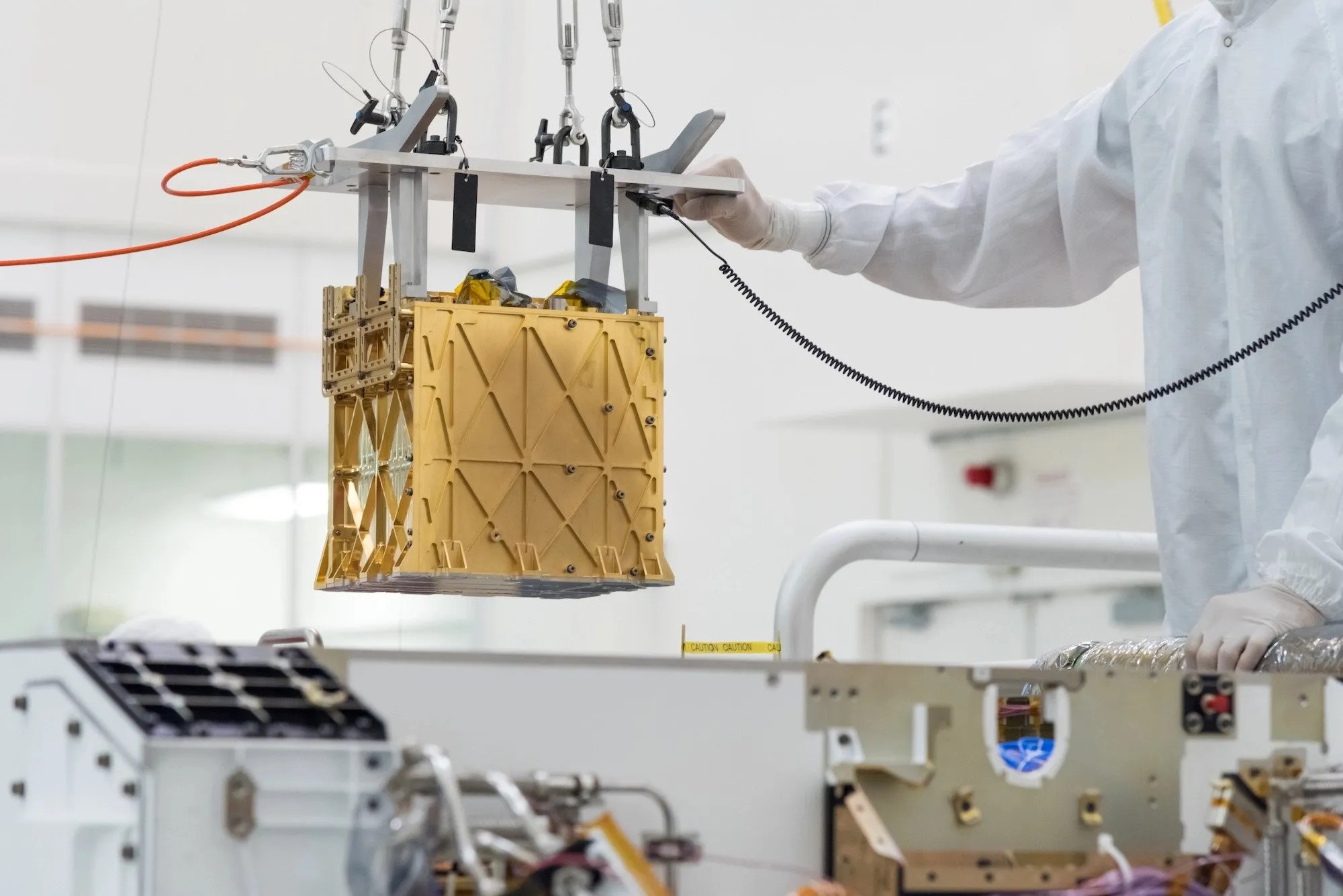 Los técnicos en la sala limpia bajan con cuidado el instrumento del Experimento de utilización de recursos in situ de oxígeno de Marte (MOXIE, por sus siglas en inglés) al vientre del Rover Perseverance.