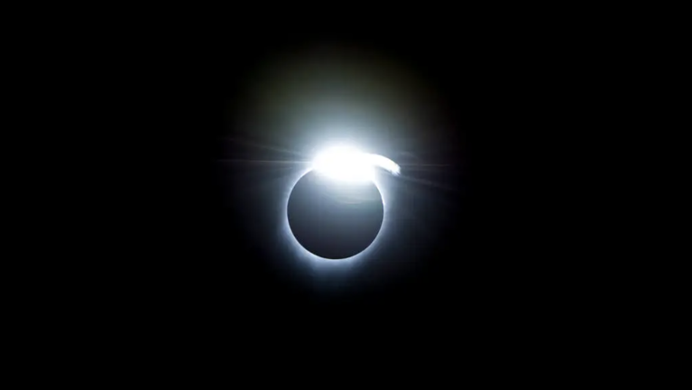 La imagen muestra un ejemplo del efecto de anillo de diamantes, que ocurrió al principio y al final de la totalidad durante un eclipse solar total el 21 de agosto de 2017. Un halo blanco y muy brillante rodea la figura del Sol eclipsado, más notablemente arriba y en el centro. El fondo es negro.