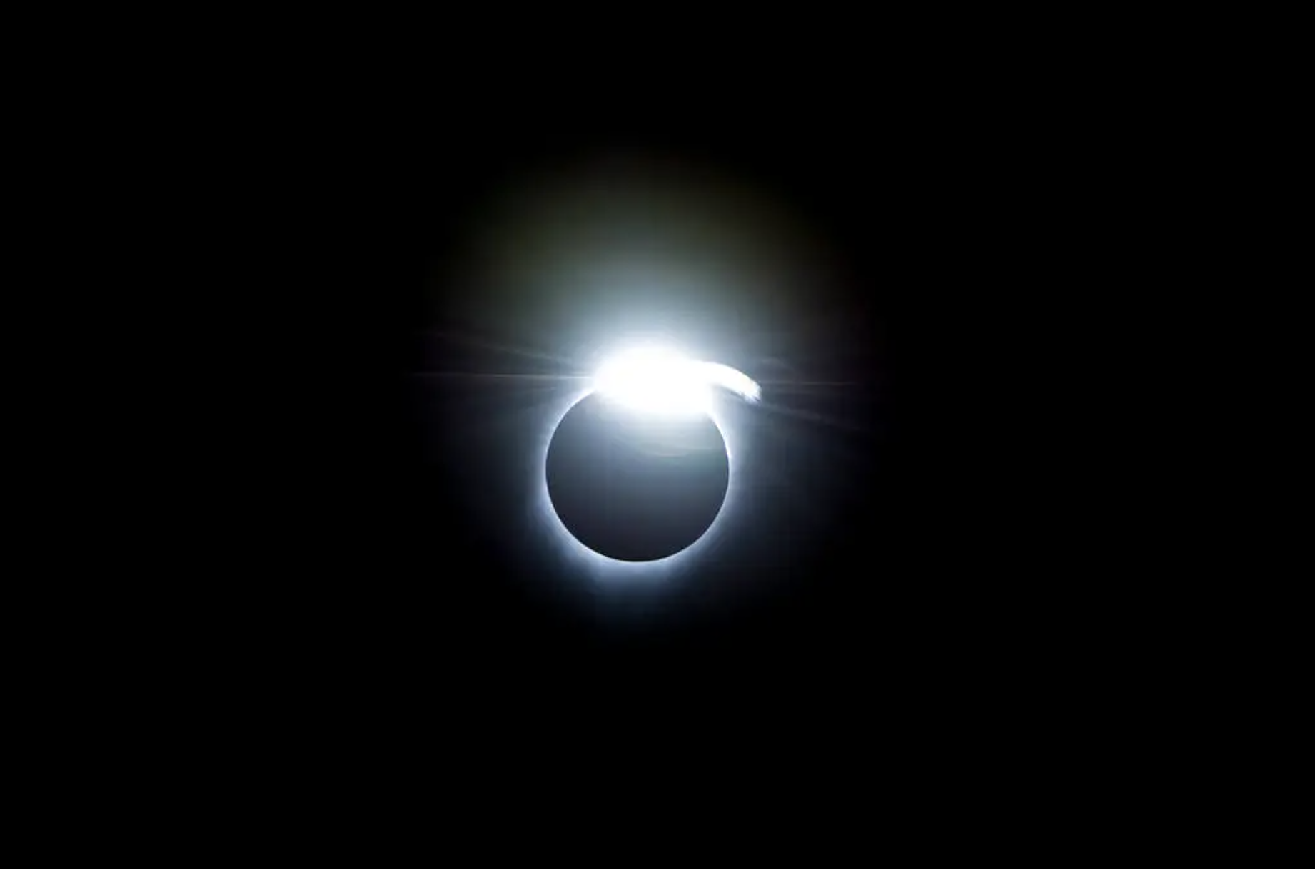 La imagen muestra un ejemplo del efecto de anillo de diamantes, que ocurrió al principio y al final de la totalidad durante un eclipse solar total el 21 de agosto de 2017. Un halo blanco y muy brillante rodea la figura del Sol eclipsado, más notablemente arriba y en el centro. El fondo es negro.