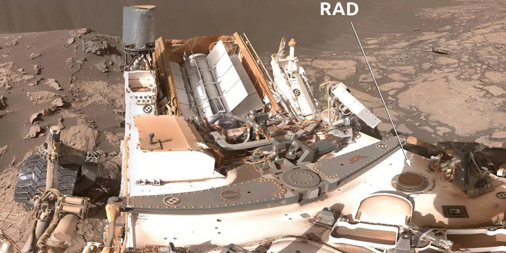 En esta imagen, se señala con una flecha blanca el Detector de Evaluación de Radiación (RAD) a bordo del vehículo explorador Curiosity de la NASA, ubicado en la parte posterior del rover.
