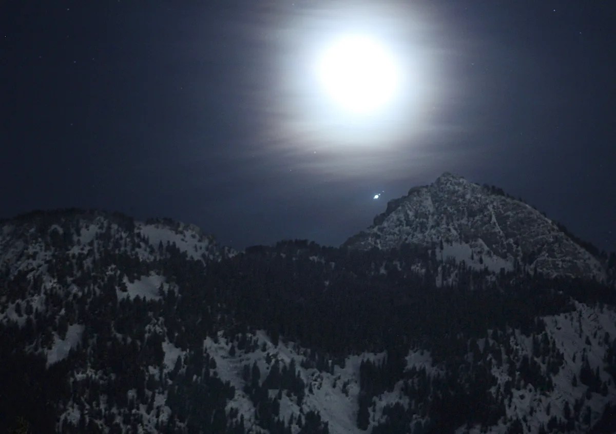 Una luna gibosa creciente, perdida en la neblina, se eleva sobre las montañas Wasatch cerca de Salt Lake City el 27 de febrero de 2019. Cerca de ella, se puede ver el planeta Júpiter, junto con tres de sus lunas más grandes. De izquierda a derecha, son Europa, Ganímedes y Calisto. La luna Ío de Júpiter también está incluida dentro del encuadre, pero a esta escala se pierde en el resplandor del planeta gigante.