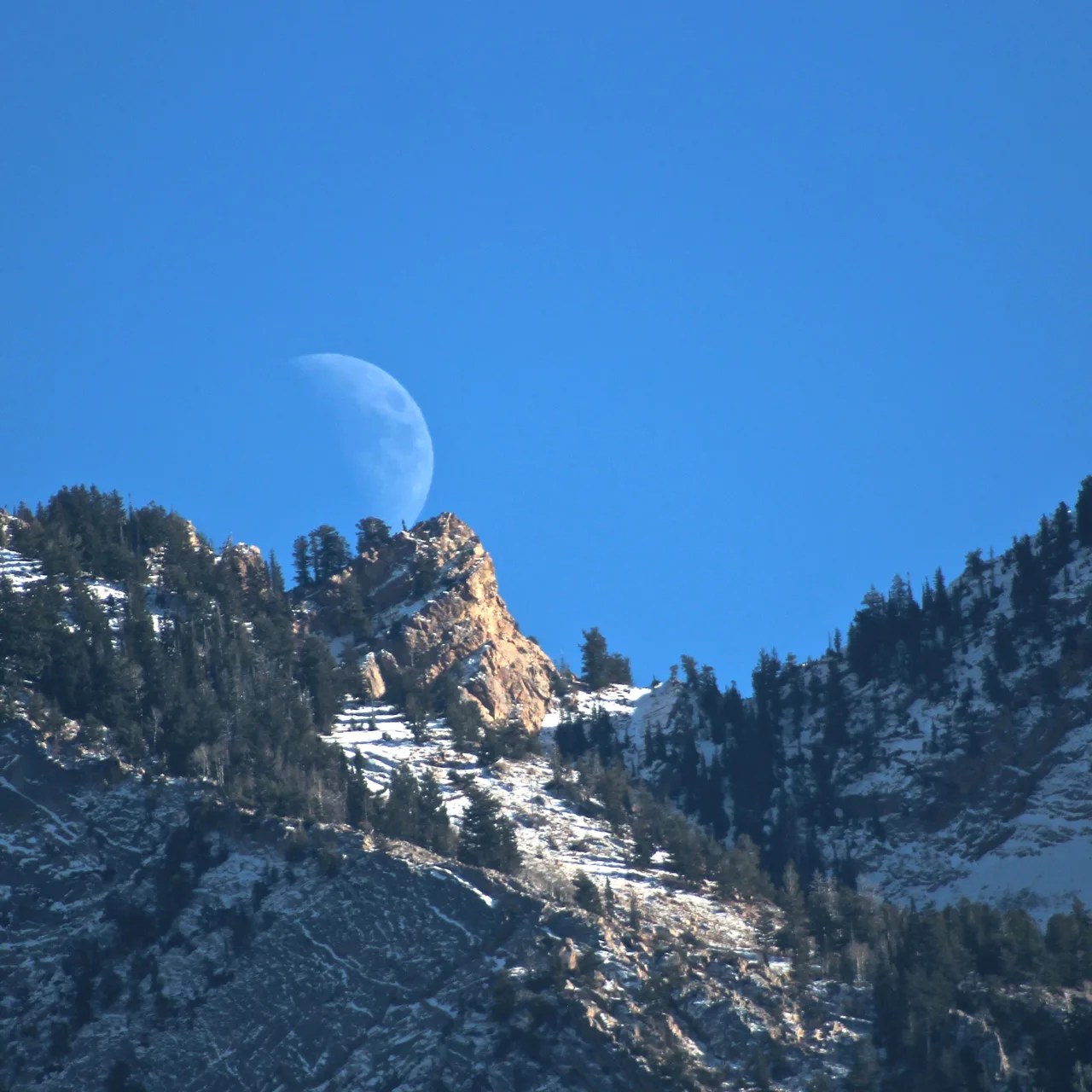 Una luna creciente se eleva sobre una cumbre en las montañas Wasatch, Utah.