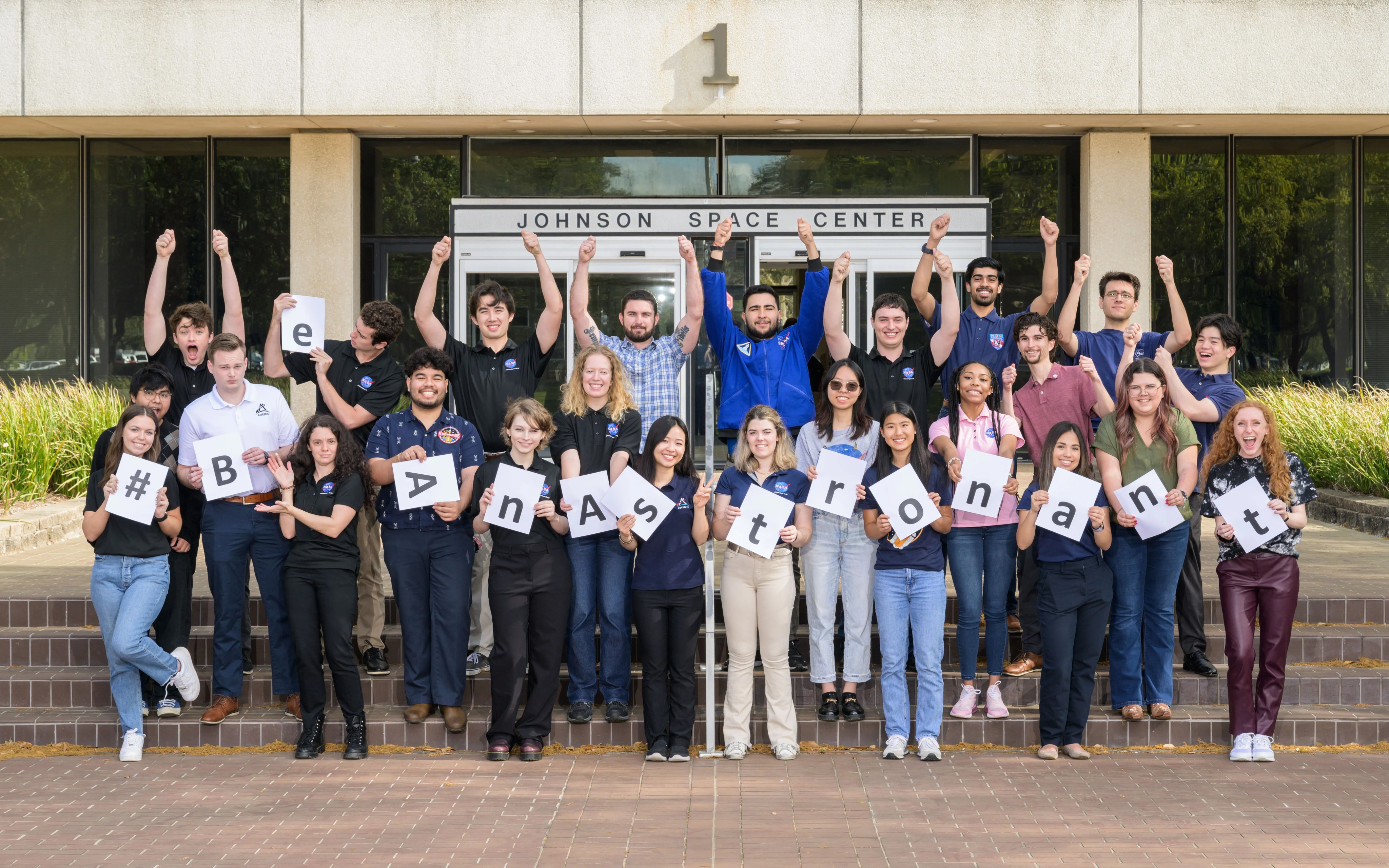 Estudiantes en pasantías del Centro Espacial Johnson sostienen un cartel para animar a la nueva generación de exploradores a postularse para el programa #BeAnAstronaut (#SerAstronauta).